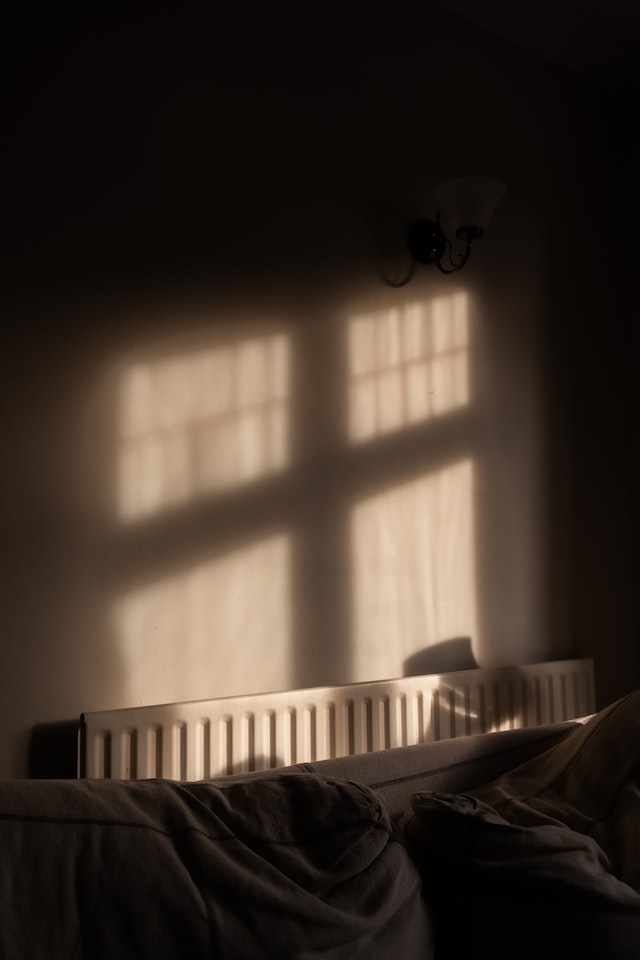 German radiator next to bed with window silhouette overshadowing the radiator